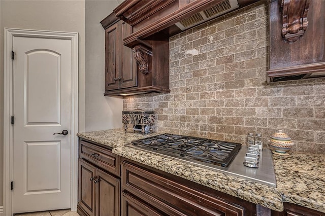 kitchen with tasteful backsplash, light stone countertops, stainless steel gas cooktop, and dark brown cabinets