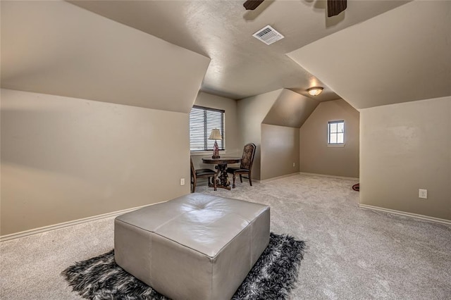 living area featuring carpet, visible vents, vaulted ceiling, and a ceiling fan
