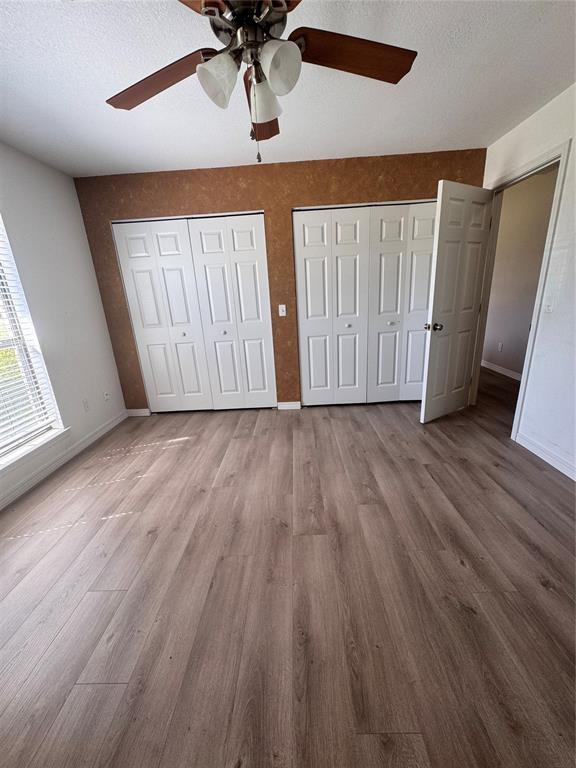 705 Cambridge Dr, Sulphur, OK 73086 - unfurnished bedroom featuring wood finished floors, baseboards, a textured ceiling, and two closets