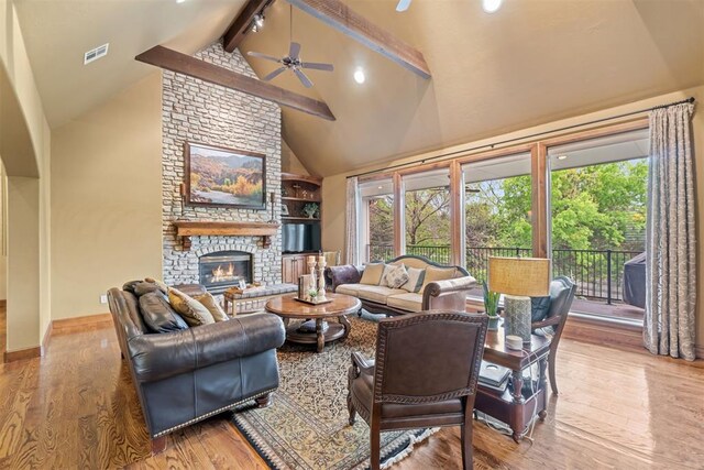3920 Creek Bank Dr, Edmond, OK 73003 - living room featuring beamed ceiling, high vaulted ceiling, ceiling fan, wood finished floors, and a stone fireplace