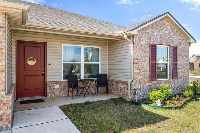 view of exterior entry featuring a yard, brick siding, and a shingled roof