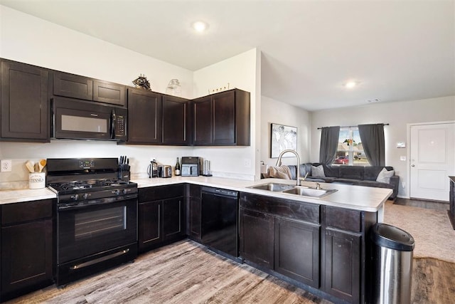 kitchen with open floor plan, a peninsula, light countertops, black appliances, and a sink