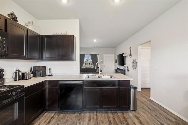 kitchen featuring a sink, light countertops, a peninsula, black appliances, and light wood finished floors