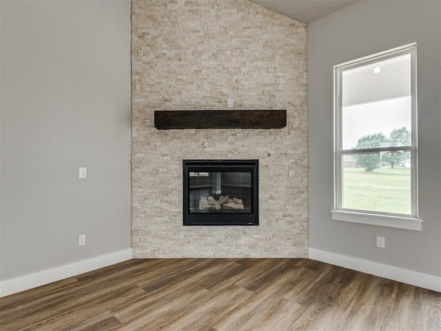 unfurnished living room with baseboards, wood finished floors, vaulted ceiling, and a stone fireplace