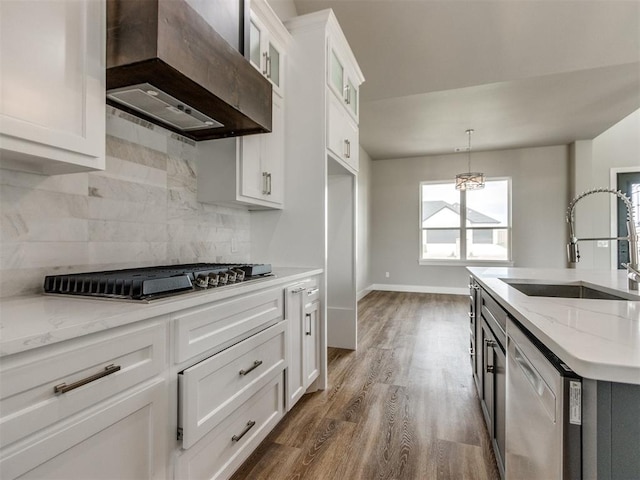 kitchen featuring wall chimney range hood, tasteful backsplash, a sink, stainless steel appliances, and white cabinetry