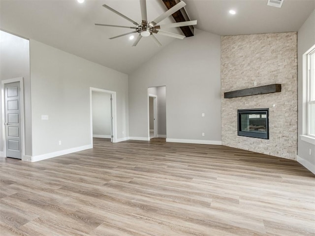unfurnished living room with ceiling fan, a fireplace, beam ceiling, high vaulted ceiling, and light wood-style floors