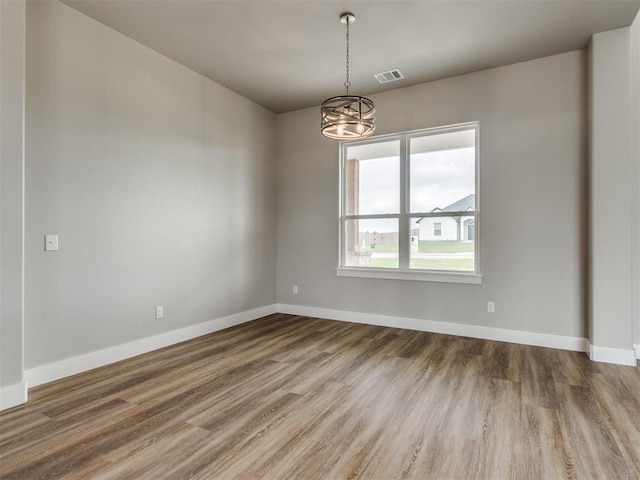 empty room with baseboards, visible vents, wood finished floors, and a notable chandelier