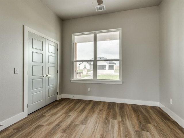 empty room with visible vents, a ceiling fan, baseboards, and wood finished floors