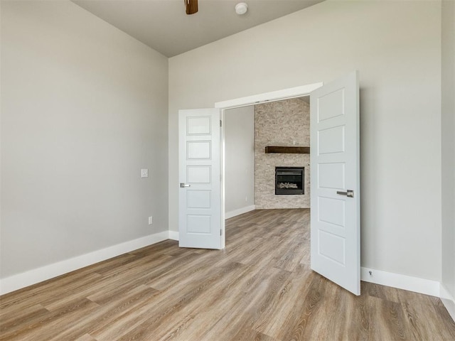 unfurnished living room featuring baseboards, a ceiling fan, wood finished floors, and a fireplace