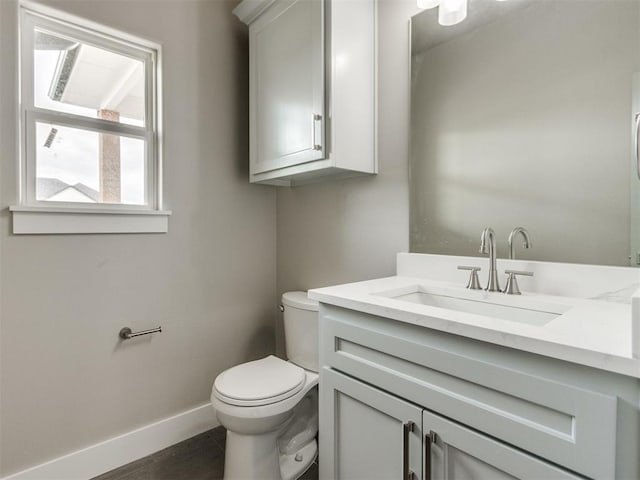 half bath featuring baseboards, vanity, toilet, and wood finished floors