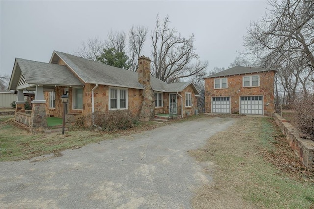 1319 S Division St, Guthrie, OK 73044 - view of front of home with stone siding, asphalt driveway, a chimney, an attached garage, and covered porch
