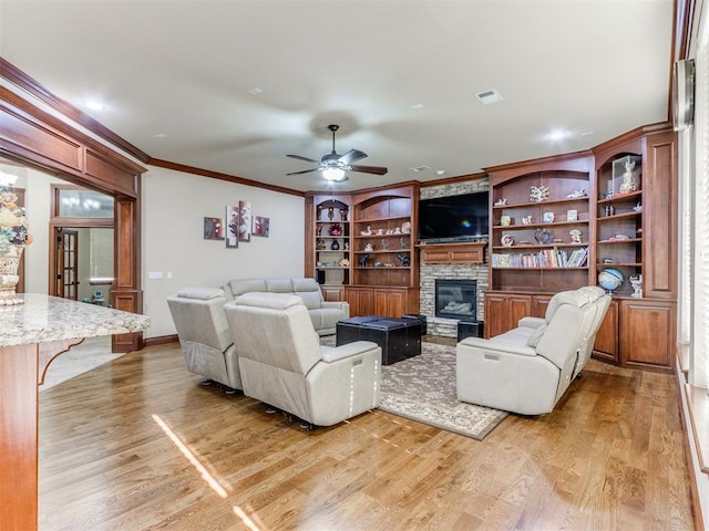 living area with crown molding, a fireplace, light wood-type flooring, a ceiling fan, and visible vents
