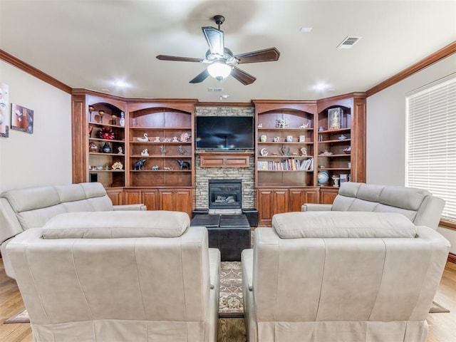 living area with visible vents, ceiling fan, light wood-type flooring, a stone fireplace, and crown molding