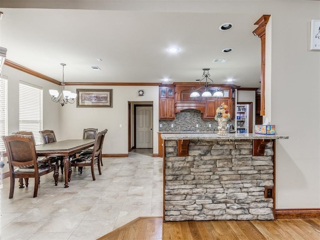 kitchen featuring a kitchen breakfast bar, baseboards, ornamental molding, glass insert cabinets, and backsplash
