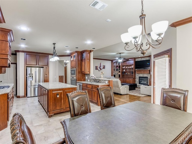 dining room with ceiling fan with notable chandelier, a fireplace, ornamental molding, visible vents, and built in shelves