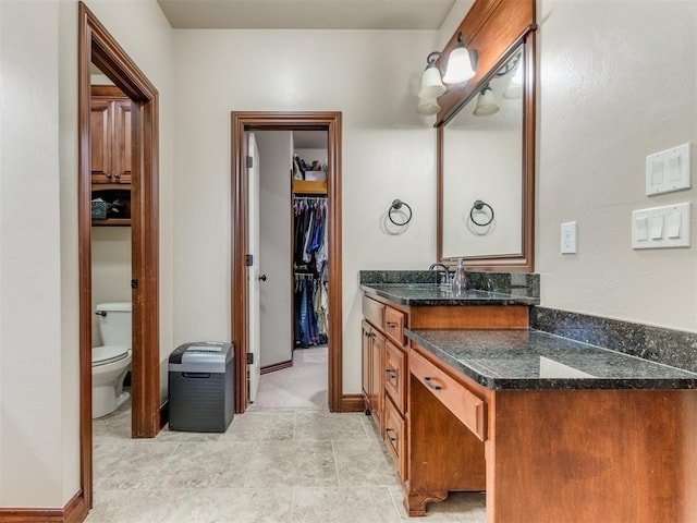 full bath with a spacious closet, toilet, vanity, and baseboards