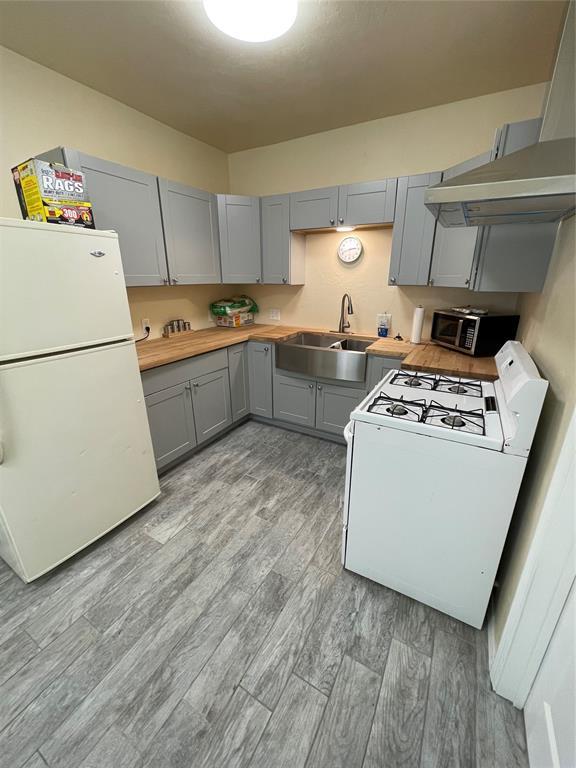 8100 NE 23rd St, Midwest City, OK 73141 - kitchen featuring gray cabinetry, a sink, light wood-style floors, under cabinet range hood, and white appliances