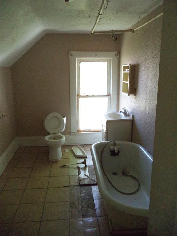 708 E Harrison Ave, Guthrie, OK 73044 - bathroom featuring a bath, tile patterned floors, a sink, toilet, and lofted ceiling