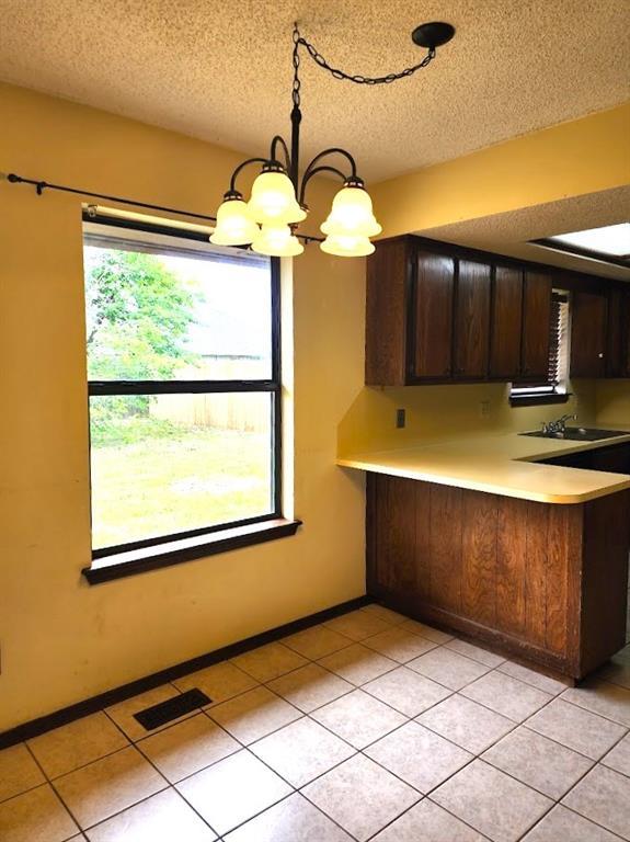 613 NE 15th St, Moore, OK 73160 - kitchen with light countertops, a textured ceiling, a chandelier, dark brown cabinets, and light tile patterned floors