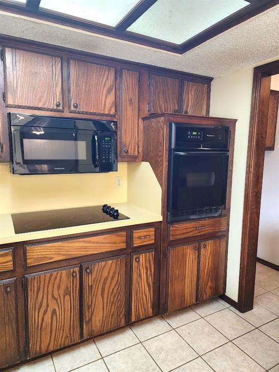 613 NE 15th St, Moore, OK 73160 - kitchen featuring black appliances, light countertops, light tile patterned floors, and a textured ceiling