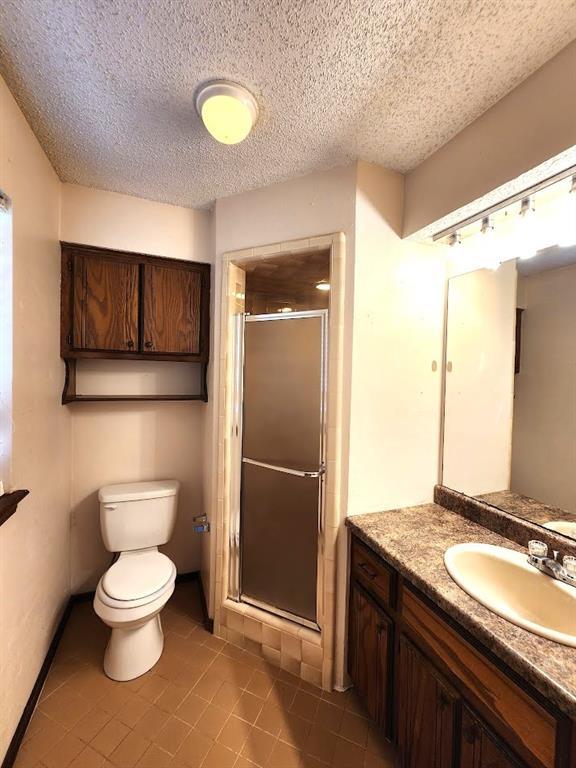 613 NE 15th St, Moore, OK 73160 - full bath featuring tile patterned flooring, toilet, a stall shower, vanity, and a textured ceiling