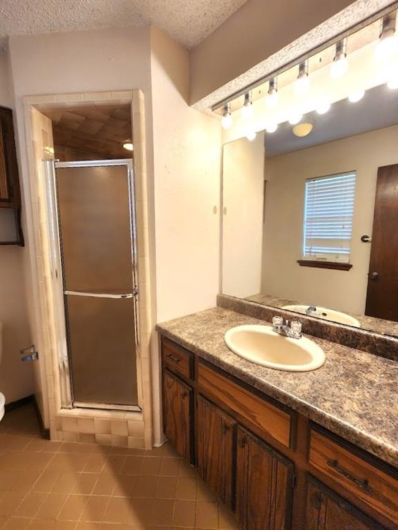 613 NE 15th St, Moore, OK 73160 - bathroom featuring tile patterned flooring, a shower stall, vanity, toilet, and a textured ceiling