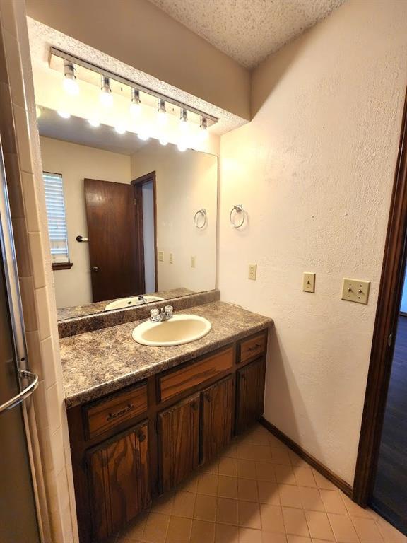 613 NE 15th St, Moore, OK 73160 - bathroom featuring vanity, a textured ceiling, tile patterned flooring, and baseboards