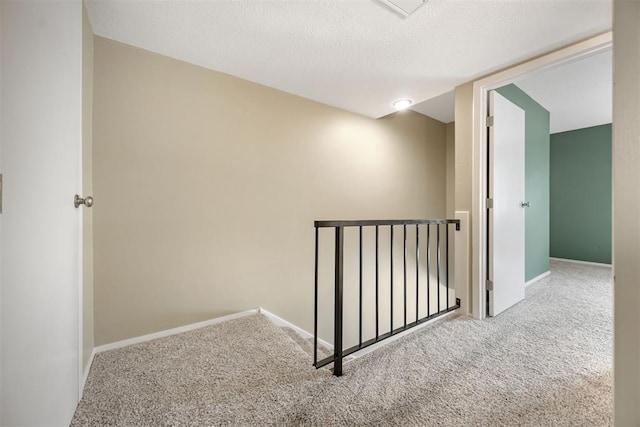 corridor with a textured ceiling, carpet flooring, baseboards, and an upstairs landing