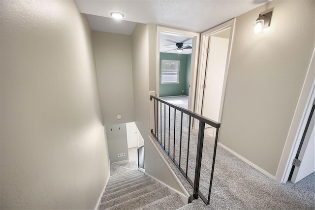 stairs featuring a textured ceiling, carpet flooring, baseboards, and ceiling fan
