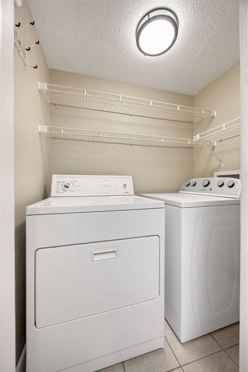 clothes washing area featuring a textured ceiling, washer and dryer, laundry area, and light tile patterned flooring