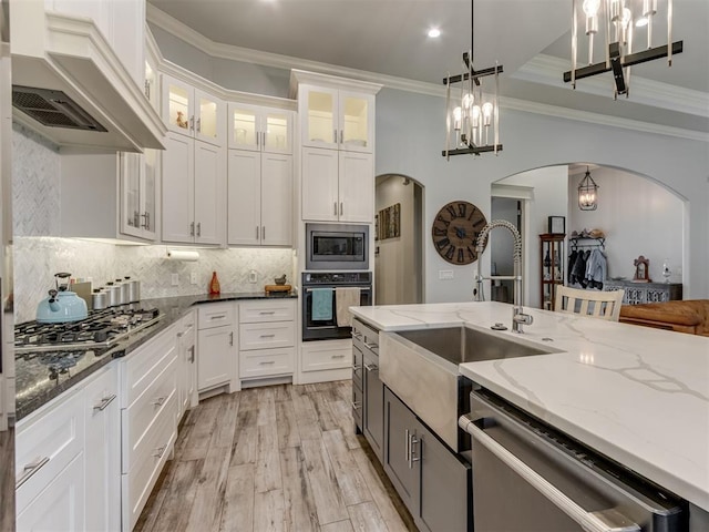 3108 Drake Crest Dr, Edmond, OK 73034 - kitchen with white cabinets, a sink, stainless steel appliances, arched walkways, and custom exhaust hood