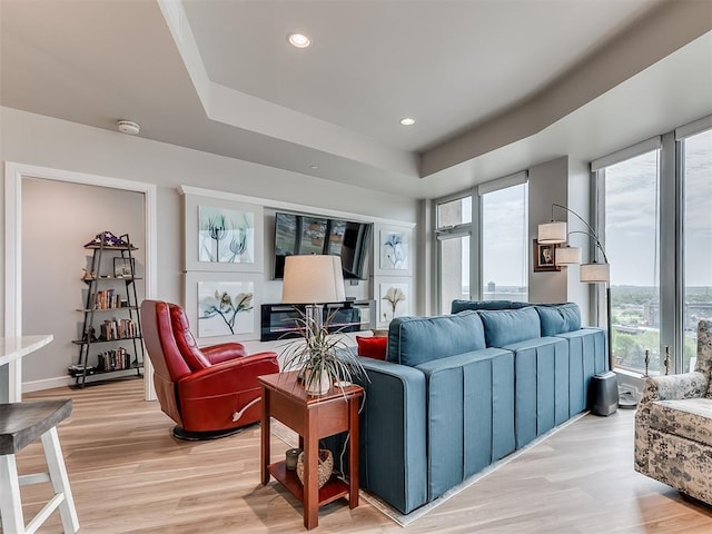 living area with light wood finished floors, recessed lighting, and a raised ceiling