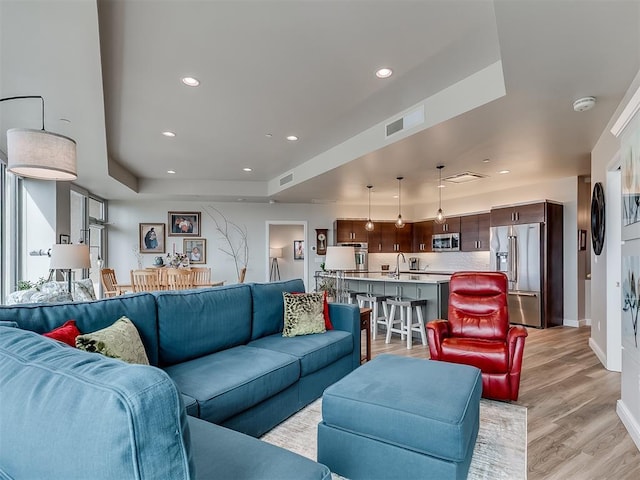 living area with light wood-style floors, a tray ceiling, baseboards, visible vents, and recessed lighting