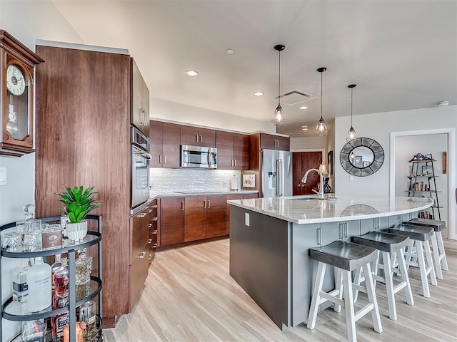 kitchen with stainless steel appliances, light wood-style flooring, a sink, visible vents, and decorative backsplash