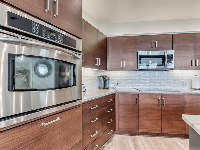 kitchen featuring light wood-type flooring, light stone countertops, backsplash, and appliances with stainless steel finishes