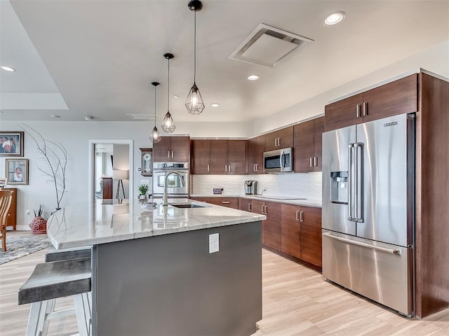 kitchen featuring a sink, decorative backsplash, a breakfast bar area, light wood finished floors, and appliances with stainless steel finishes