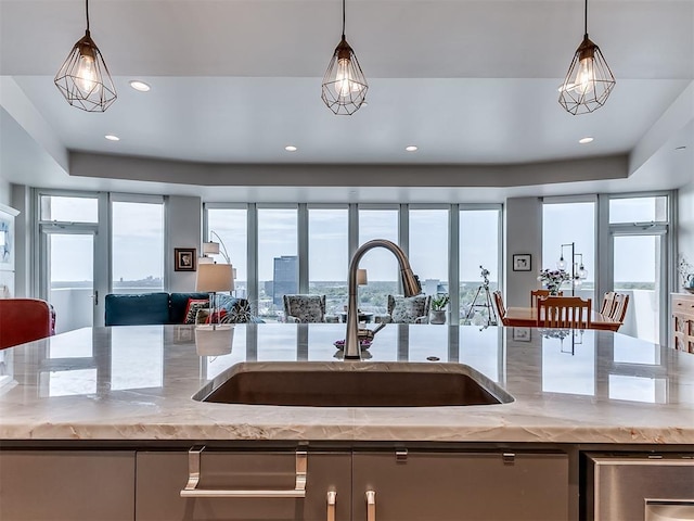 kitchen with light stone countertops, pendant lighting, open floor plan, and a sink