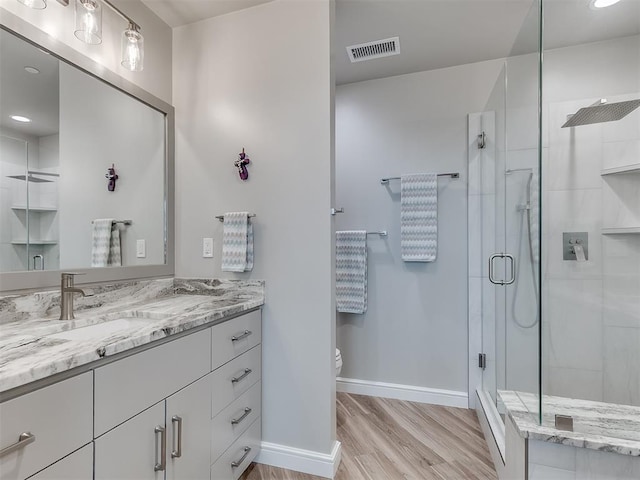 bathroom featuring wood finished floors, visible vents, vanity, baseboards, and a stall shower