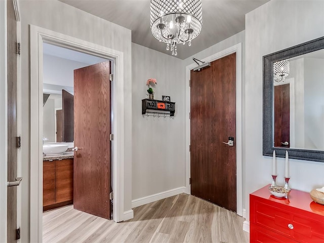 hallway with wood finished floors, baseboards, a sink, and a notable chandelier