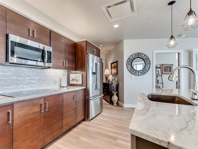 kitchen featuring stainless steel appliances, a sink, baseboards, light wood-style flooring, and hanging light fixtures