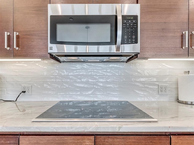 interior details with stainless steel microwave, backsplash, and black electric cooktop