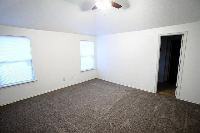 unfurnished room featuring dark carpet, a ceiling fan, vaulted ceiling, and a wealth of natural light