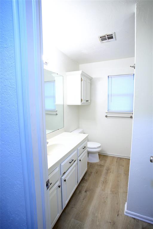 bathroom with visible vents, baseboards, toilet, vanity, and wood finished floors