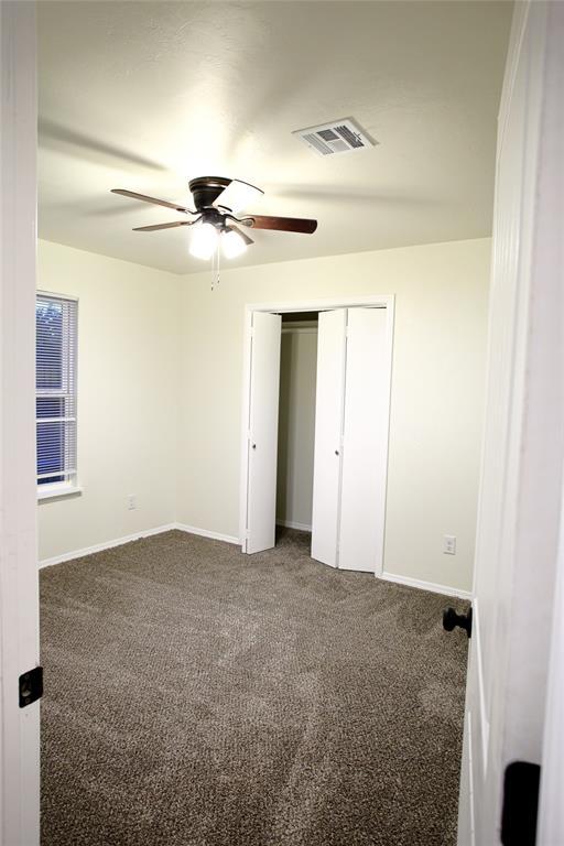 unfurnished bedroom with ceiling fan, a closet, visible vents, carpet flooring, and baseboards