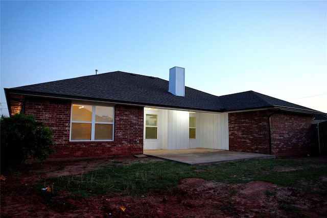 rear view of property featuring roof with shingles, a chimney, a patio area, and brick siding