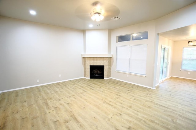 unfurnished living room with baseboards, a tiled fireplace, visible vents, ceiling fan, and wood finished floors