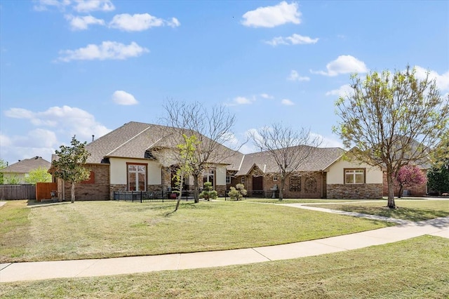 french provincial home featuring stucco siding, stone siding, a front yard, and fence