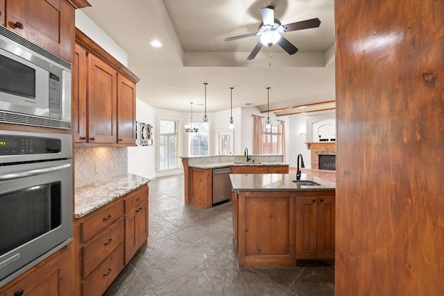 kitchen with brown cabinets, tasteful backsplash, stainless steel appliances, and ceiling fan with notable chandelier