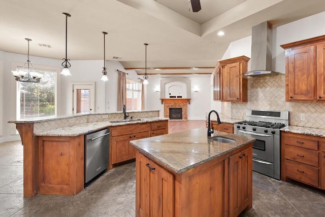 kitchen with wall chimney range hood, stainless steel appliances, a center island with sink, and a sink