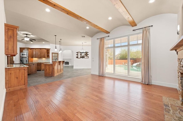 unfurnished living room with arched walkways, light wood-style flooring, baseboards, and ceiling fan with notable chandelier